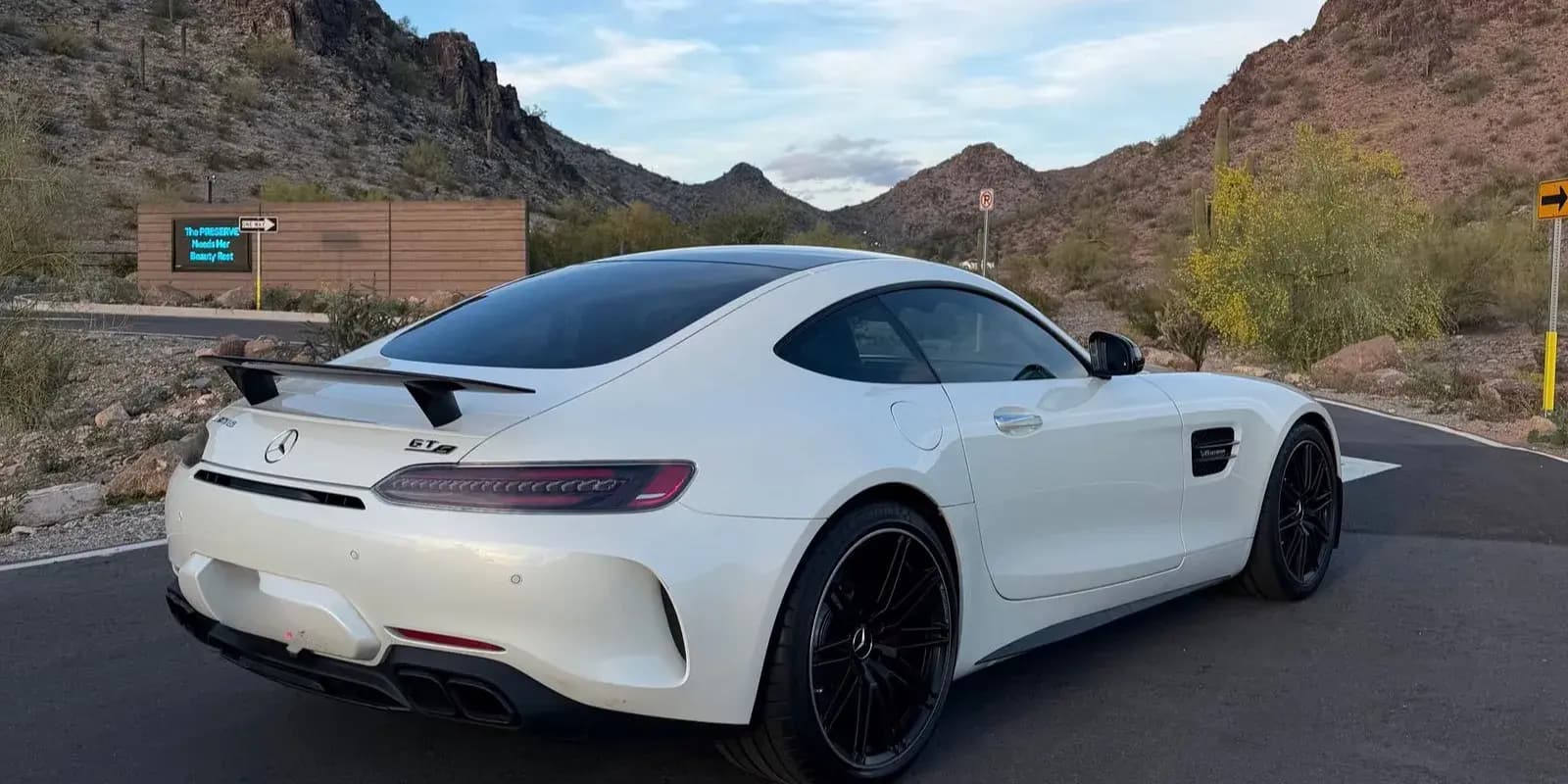 Un Mercedes-AMG GT blanco estacionado entre montanas del desierto de Arizona, recien publicado para renta